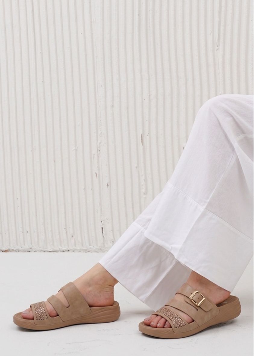 Beige sandals with gold buckles worn with white pants against a light background