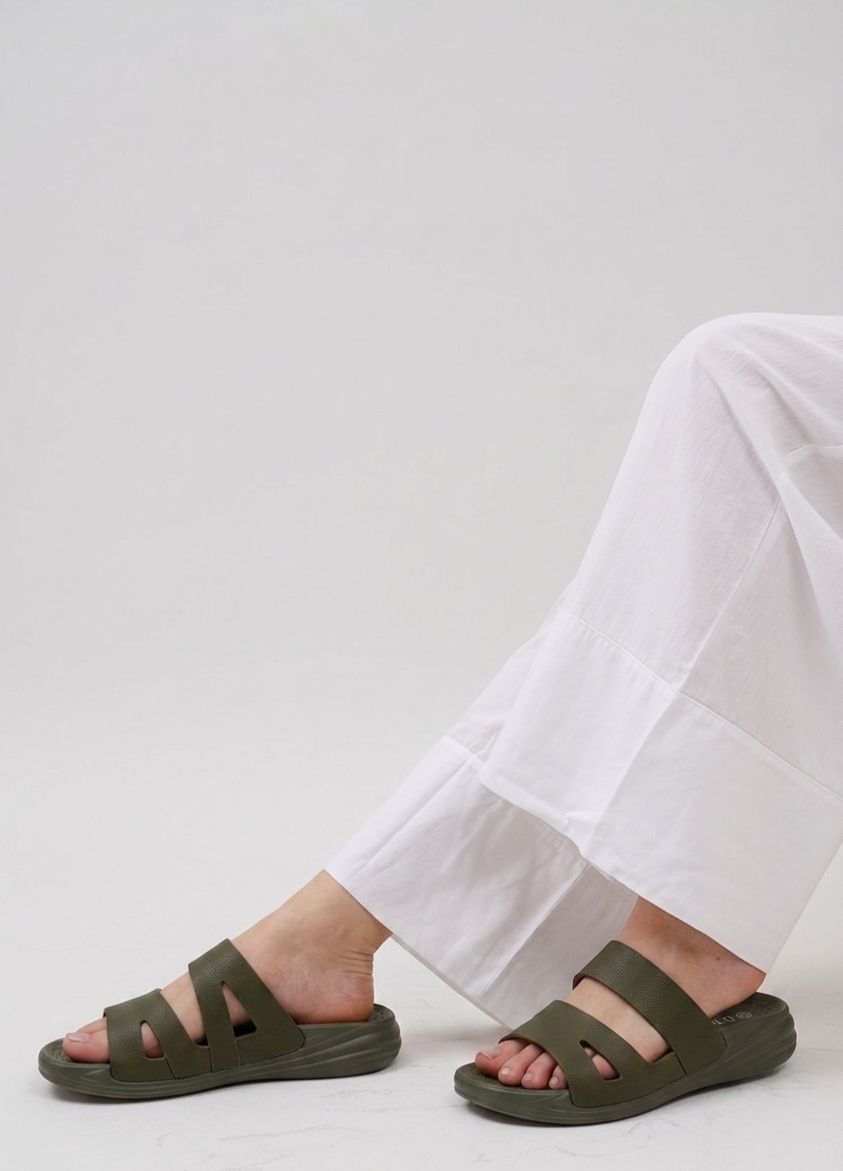 Person wearing olive green sandals with white pants on a light gray background