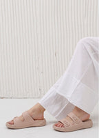 Person wearing light pink sandals and white pants on a light background