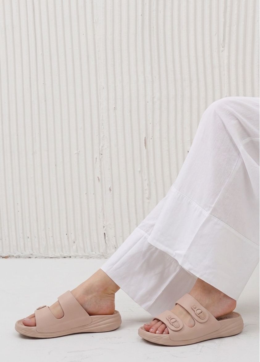 Person wearing light pink sandals and white pants on a light background