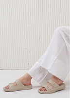 Person wearing beige sandals with a white textured background