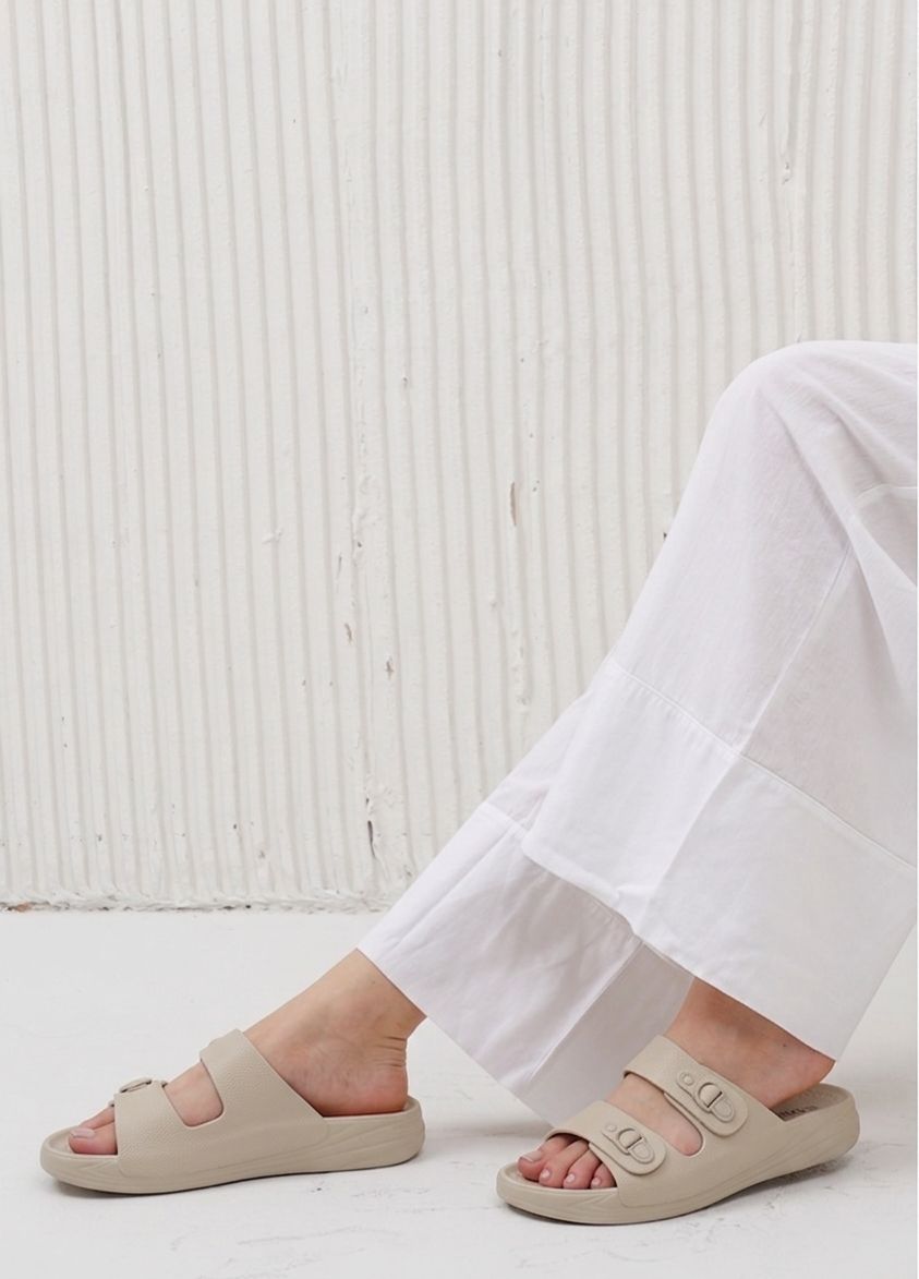 Person wearing beige sandals with a white textured background