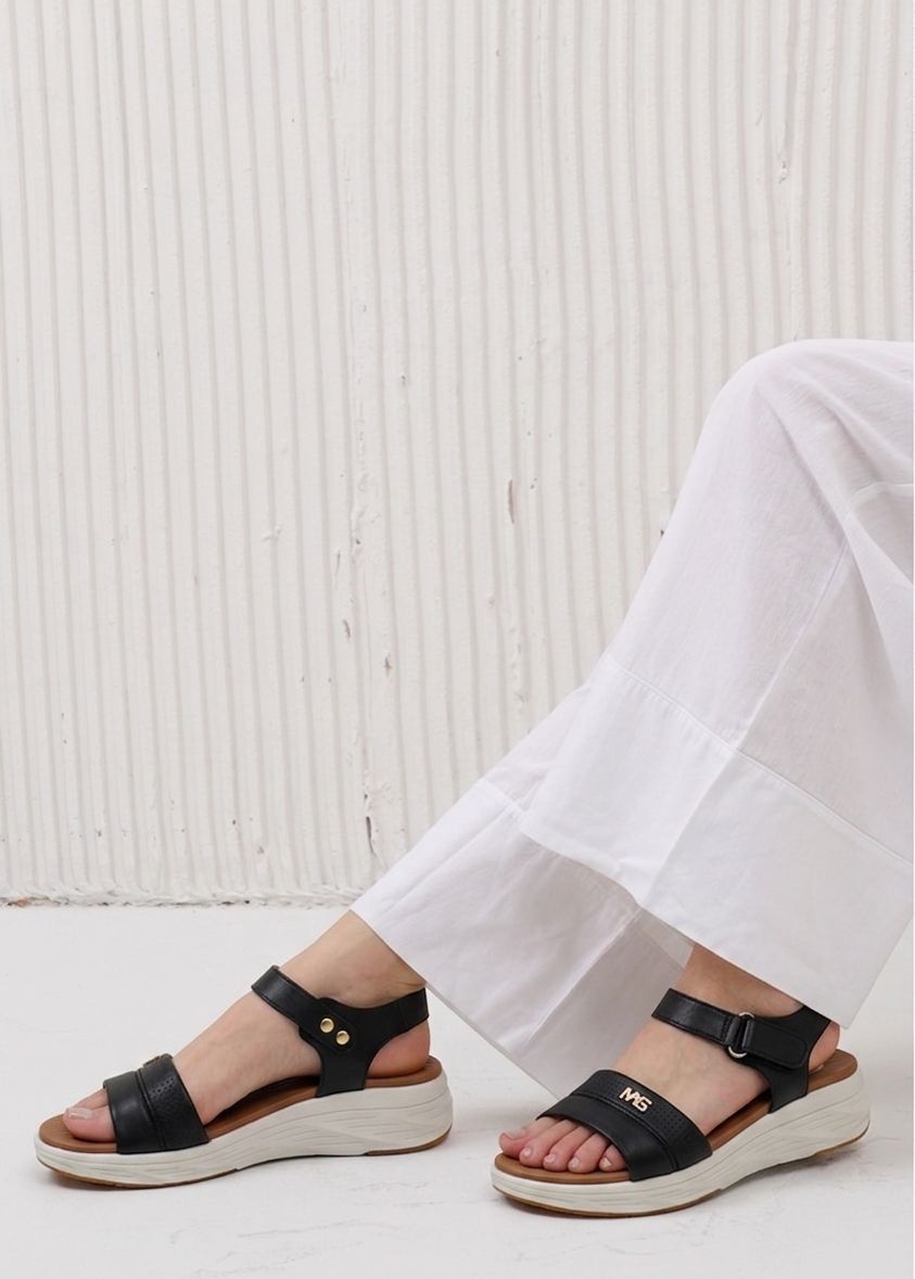 Black sandals worn with white pants against a light background