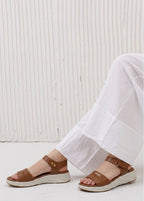 Brown sandals worn with white pants against a light background