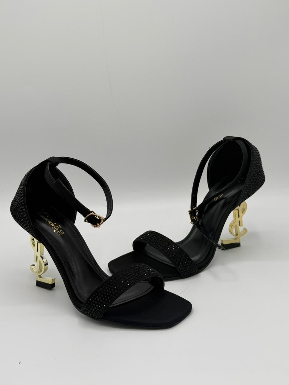 Black high-heeled sandals with gold accents on a white background