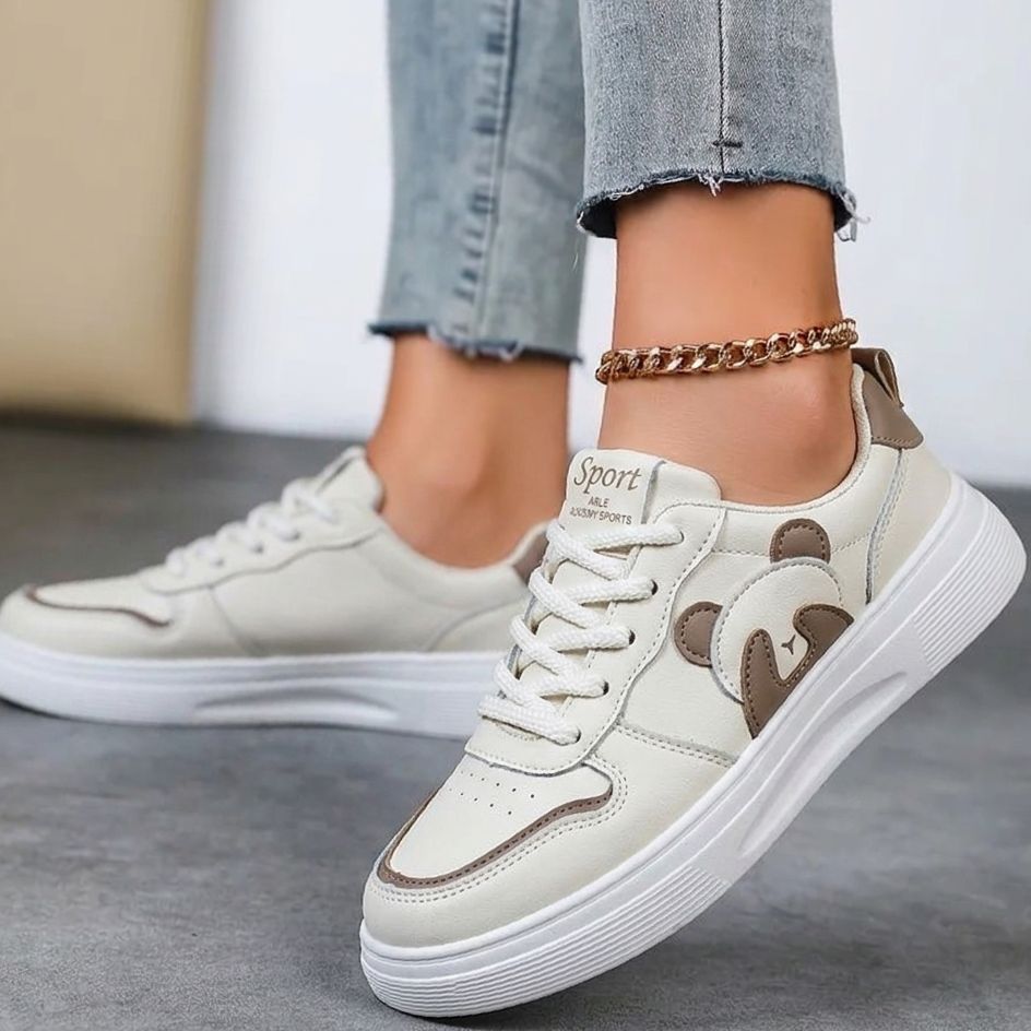 White sneakers with brown accents worn with light blue jeans on a neutral background