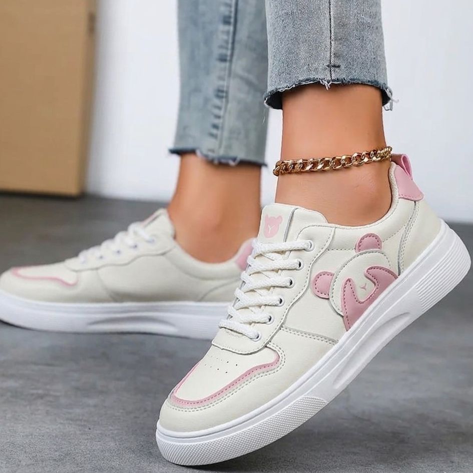 White sneakers with pink accents worn by a person on a gray floor.