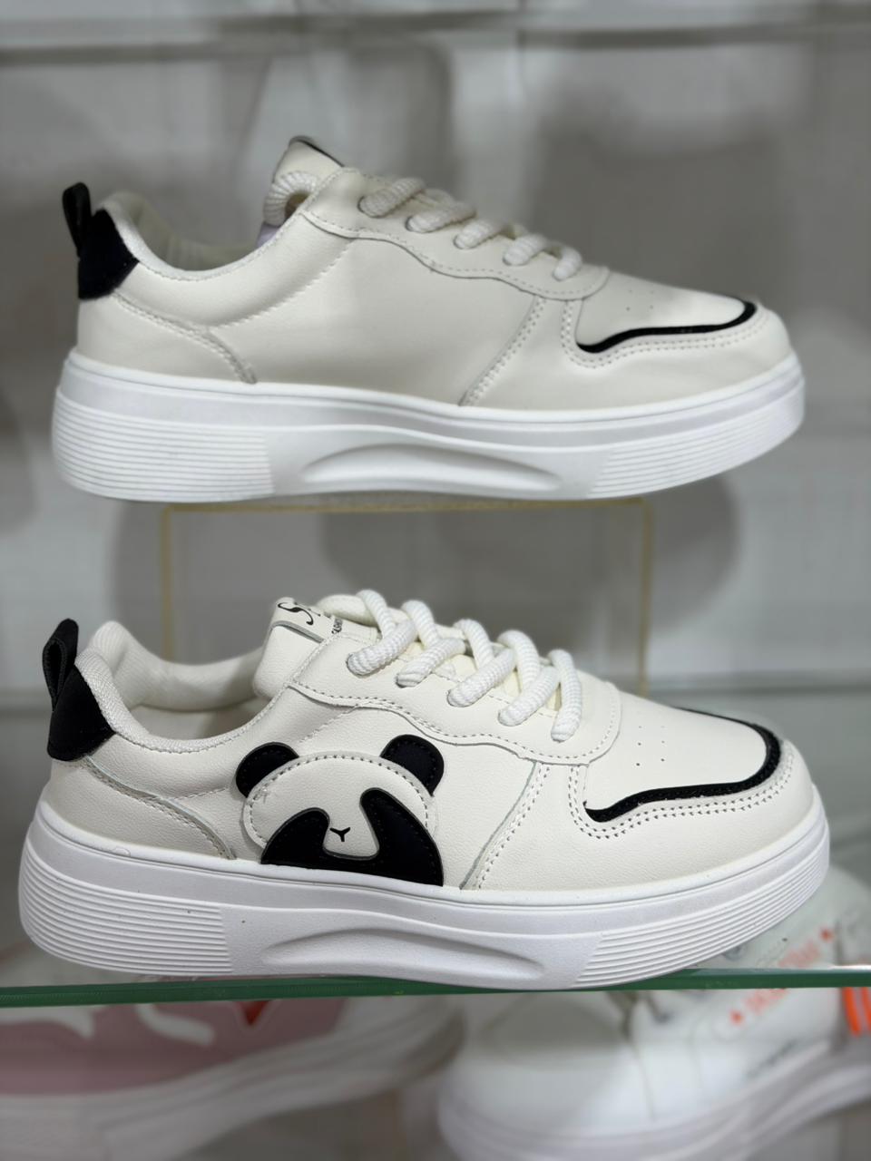 White sneakers with black panda designs on a glass surface