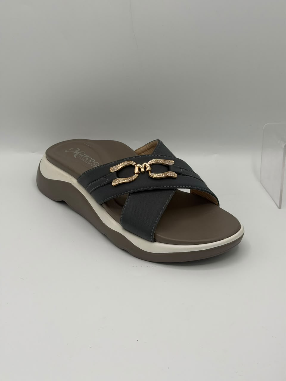 A single women's slide sandal with dark gray straps, a brown footbed, and a white midsole accent, featuring a decorative gold-tone metal buckle on the upper strap.