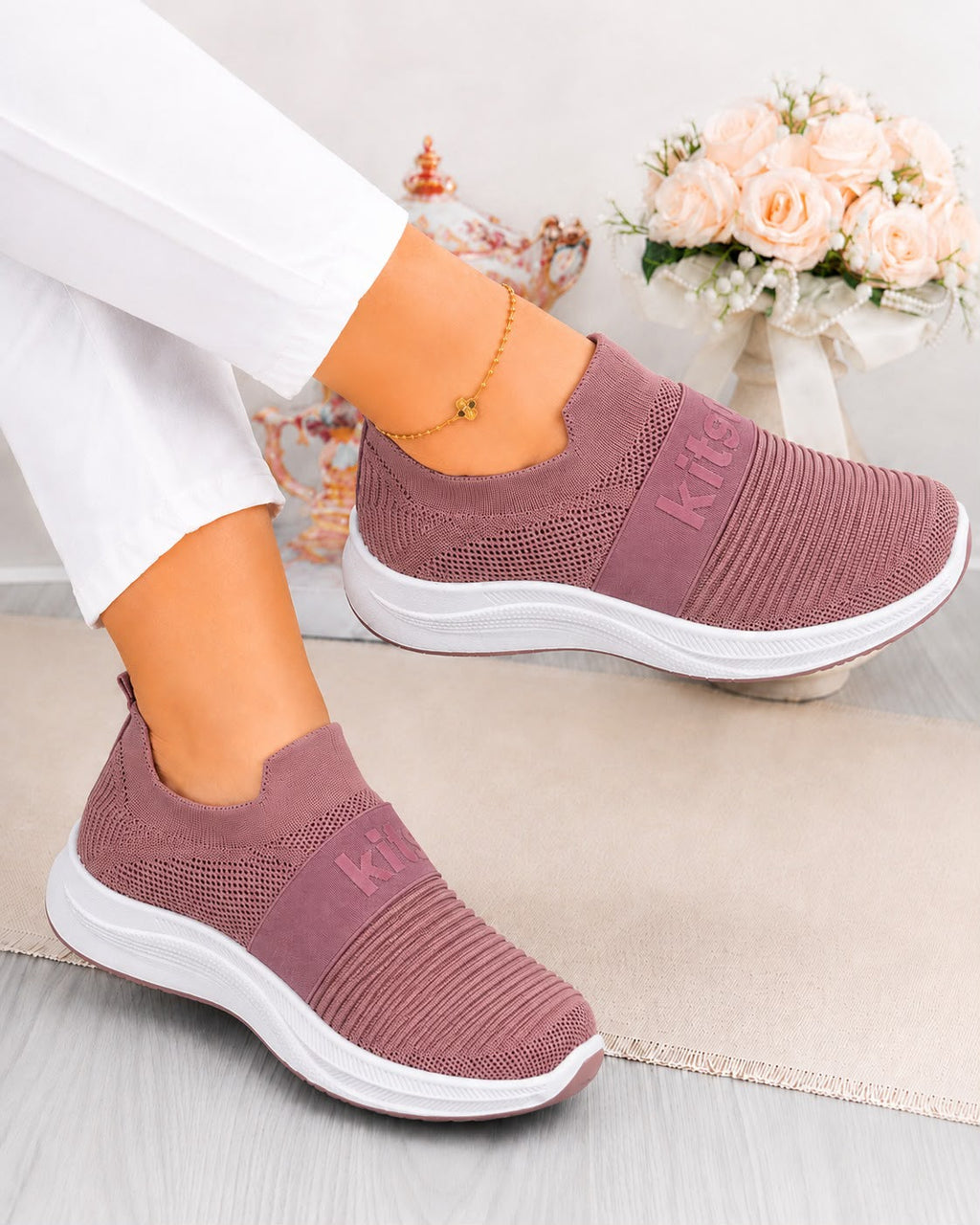 A pair of women's slip-on sneakers in a dusty rose pink color with white soles, shown on a model wearing white pants. The shoes feature a textured knit upper and a ribbed synthetic toe box, with the brand name 'Kate' visible on the side of the uppers.