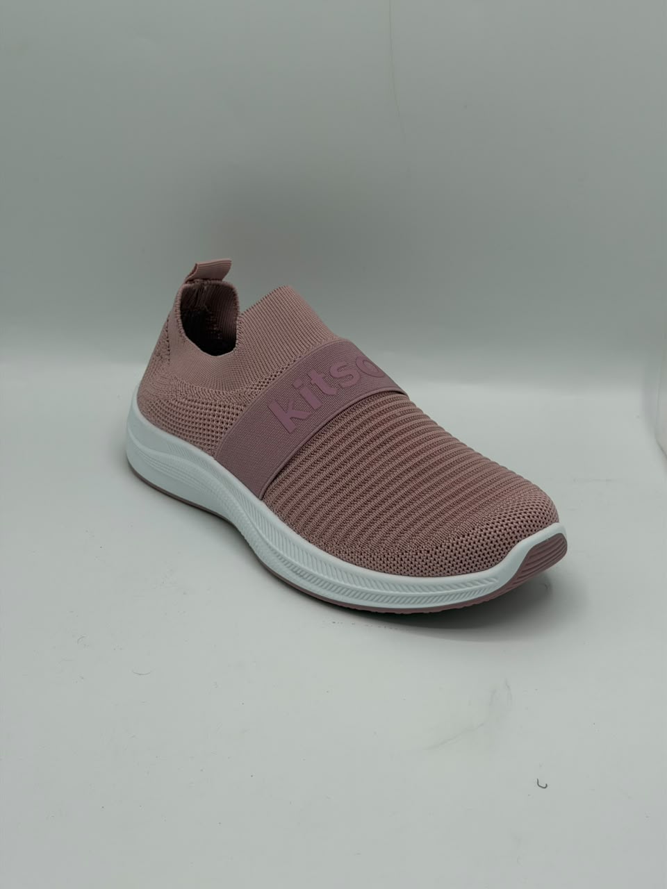 A single slip-on sneaker in dusty rose pink with a white sole, featuring a textured knit upper and a wide elastic strap with the brand name 'kits' embossed on it.