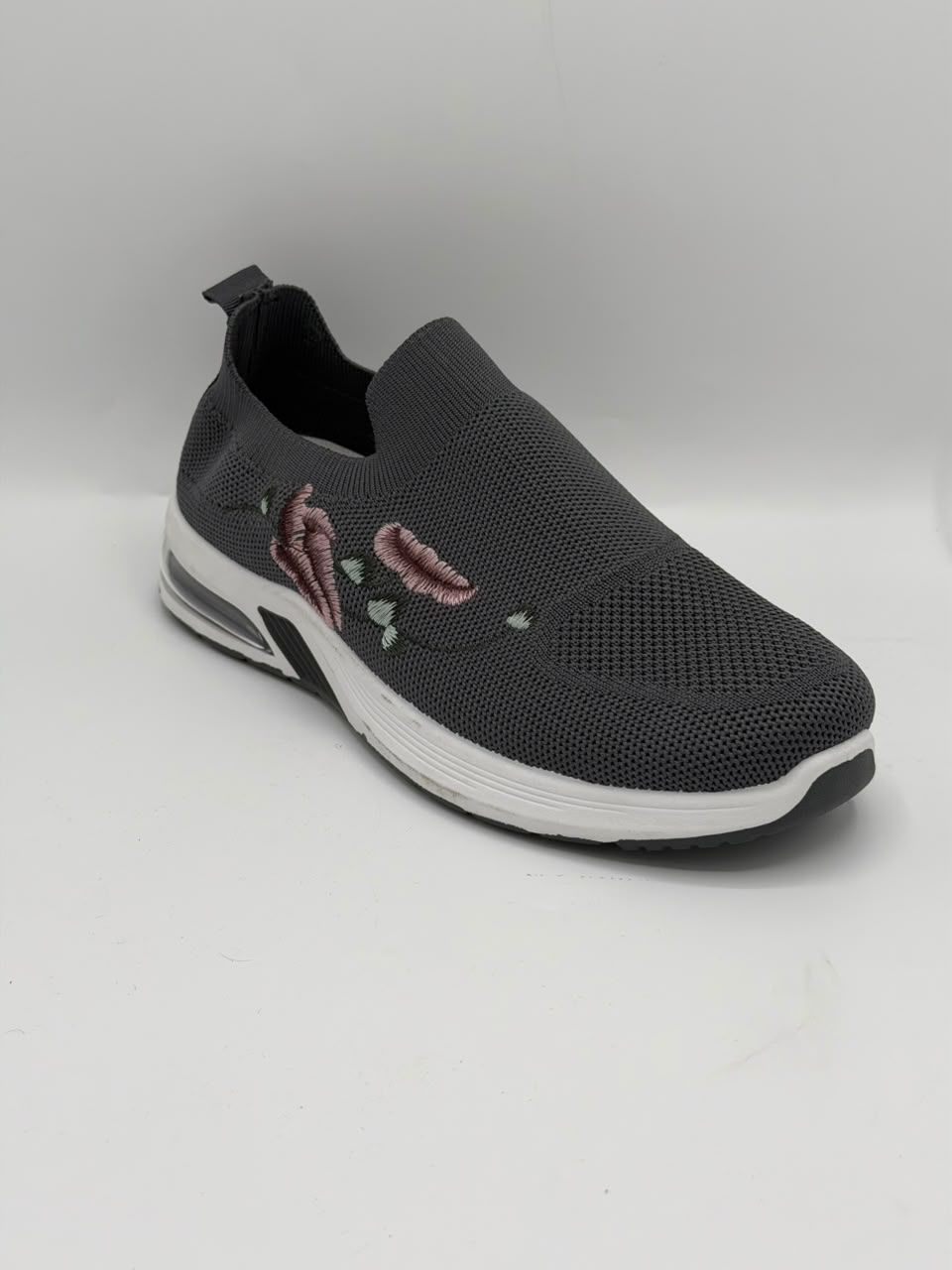 A dark gray slip-on sneaker with a textured mesh upper, featuring a pink and white floral design on the side, a white midsole, and a black outsole.