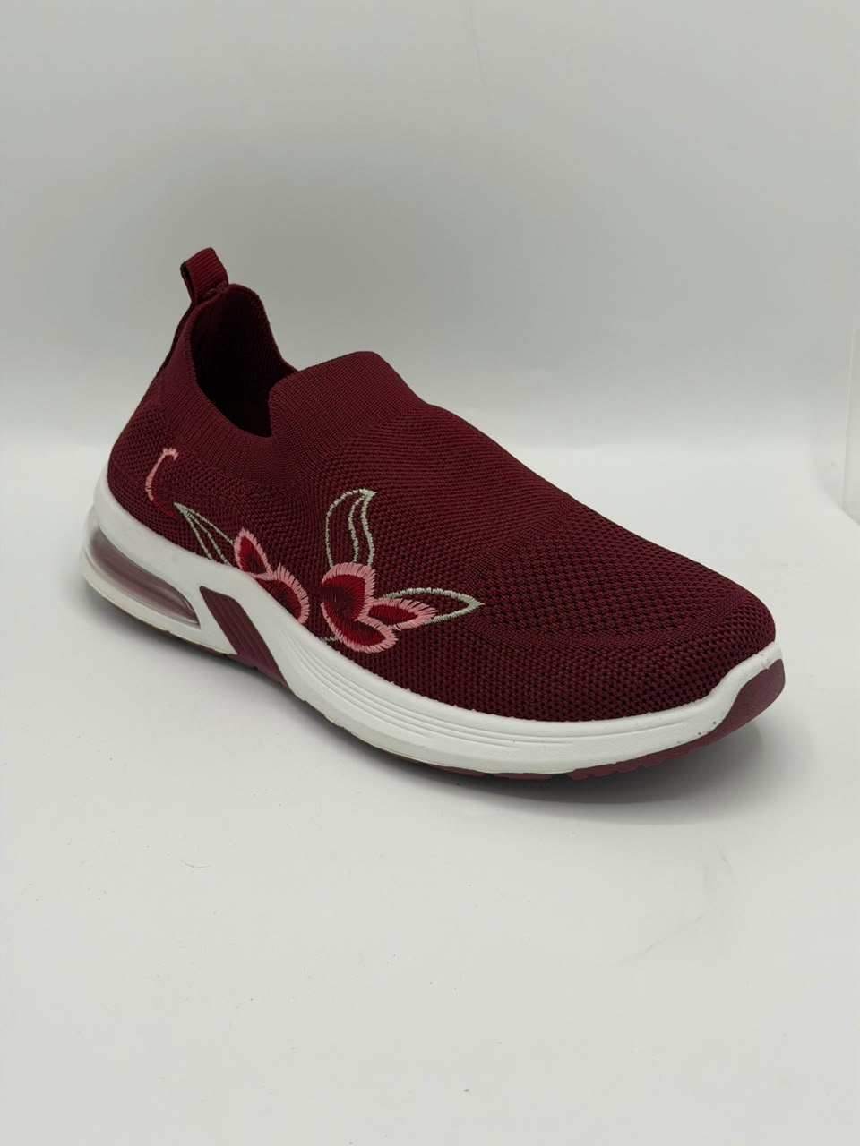 A maroon slip-on mesh sneaker with a white sole and a pink and white embroidered lotus flower on the side, shown against a plain light gray background.