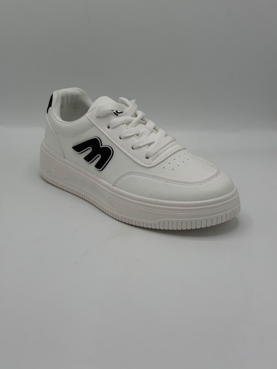 A white low-top sneaker with a thick white platform sole, featuring a black stylized 'm' logo on the side, white laces, and a white padded collar, shown against a neutral gray background.
