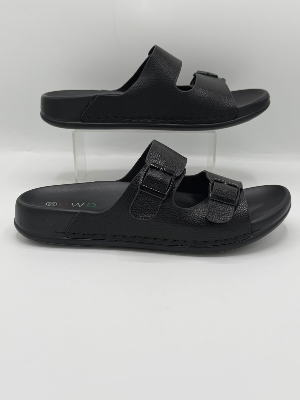 A pair of black double-strap slide sandals displayed on clear acrylic risers against a light gray background.