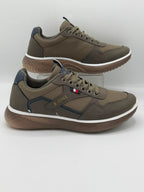 A pair of X-ONE casual sneakers in brown and dark gray with navy blue accents, displayed on a light gray background with one shoe standing on a clear display block.