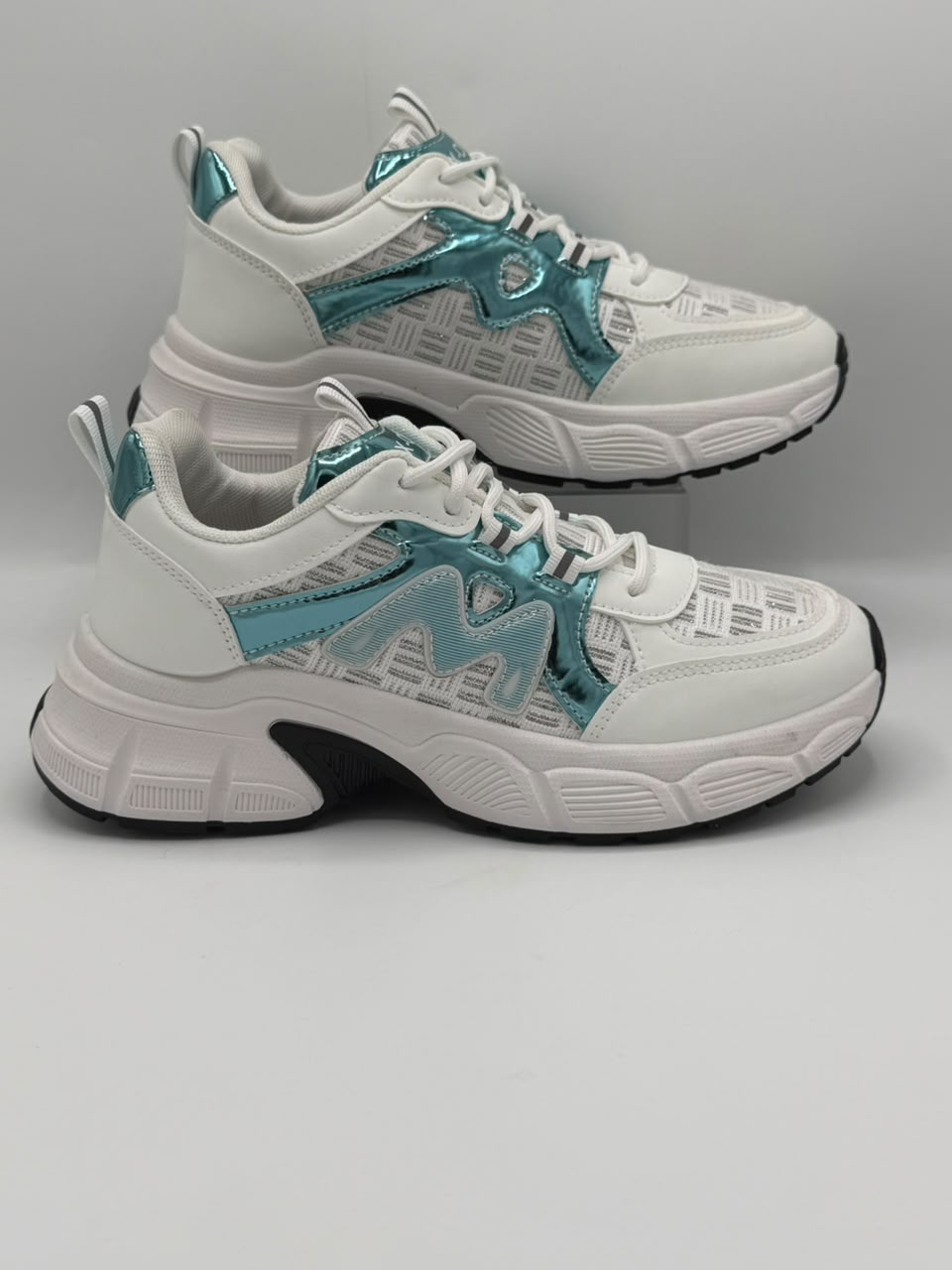 A pair of chunky white sneakers with metallic teal accents and a subtle geometric pattern, displayed on a neutral gray background.