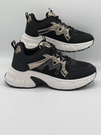 A pair of black and white chunky platform sneakers with metallic silver accents, displayed on a light gray background.