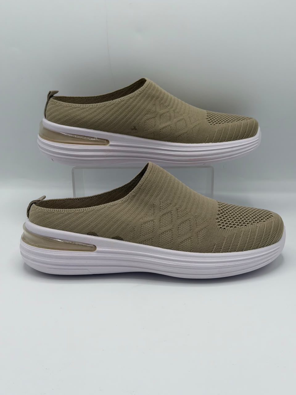A pair of slip-on wedge sneakers in olive green with textured knit uppers and thick white platform soles, displayed on a light gray background with one shoe on a clear stand.