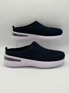 A pair of women's slip-on mule sneakers in navy blue with textured knit uppers, white soles, and a clear plastic support stand, set against a plain light gray background.