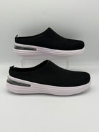 A pair of black slip-on mule sneakers with thick white platform soles and a clear heel accent, displayed on a light gray background.