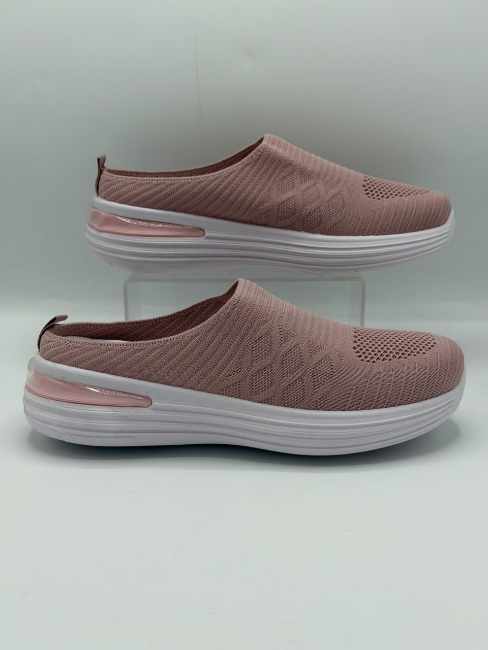 A pair of women's slip-on wedge sneakers in dusty rose pink with textured knit uppers, white soles, and a translucent pink heel accent, displayed on a light gray background with one shoe on a clear stand.