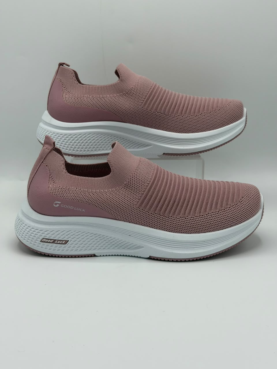 A pair of slip-on athletic sneakers in dusty rose pink with textured knit uppers and thick white midsoles, displayed against a light gray background.