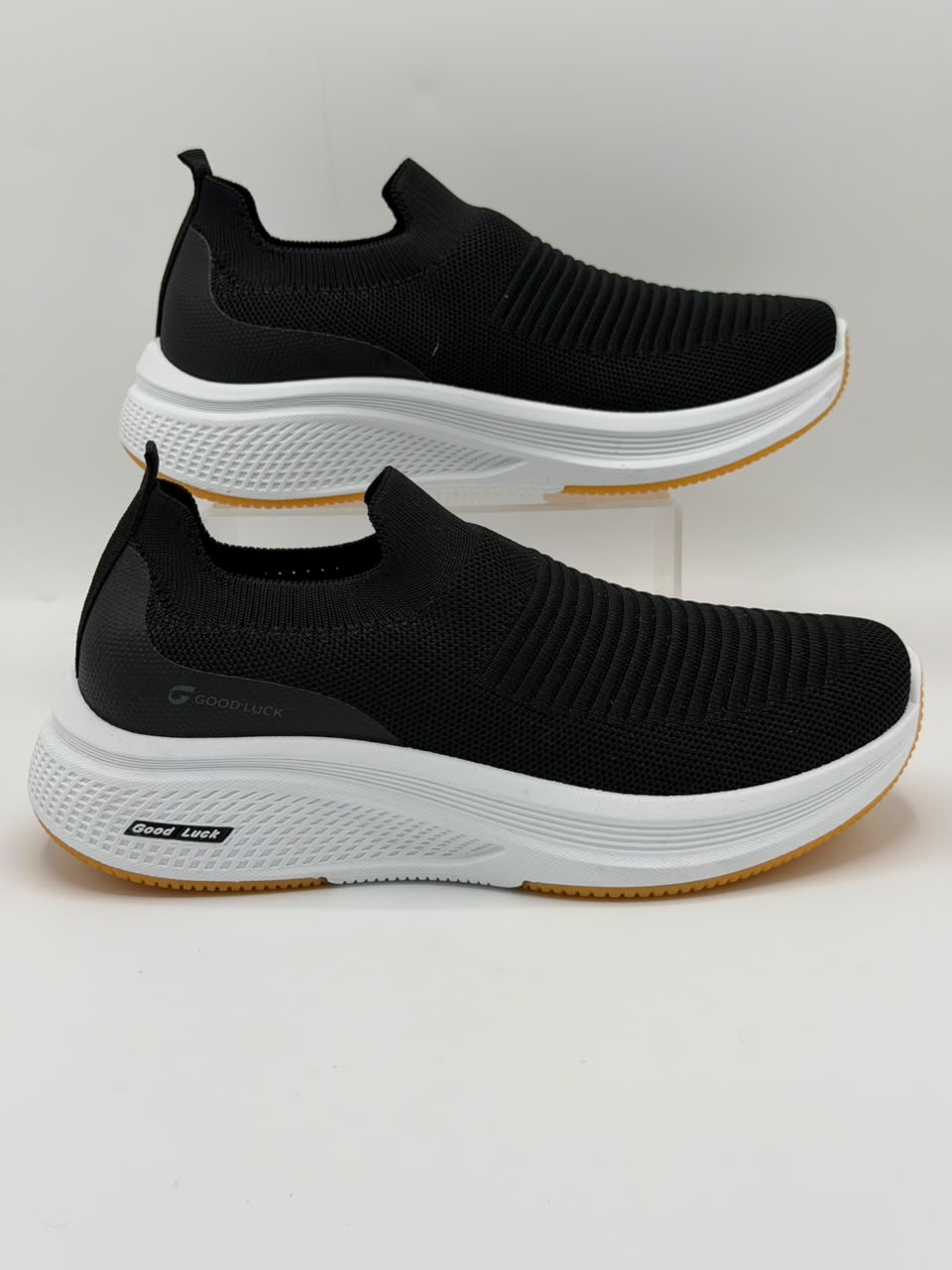A pair of black slip-on athletic sneakers with thick white midsoles and a gum outsole, displayed on a light gray background.