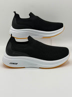A pair of black slip-on athletic sneakers with thick white midsoles and a gum outsole, displayed on a light gray background.