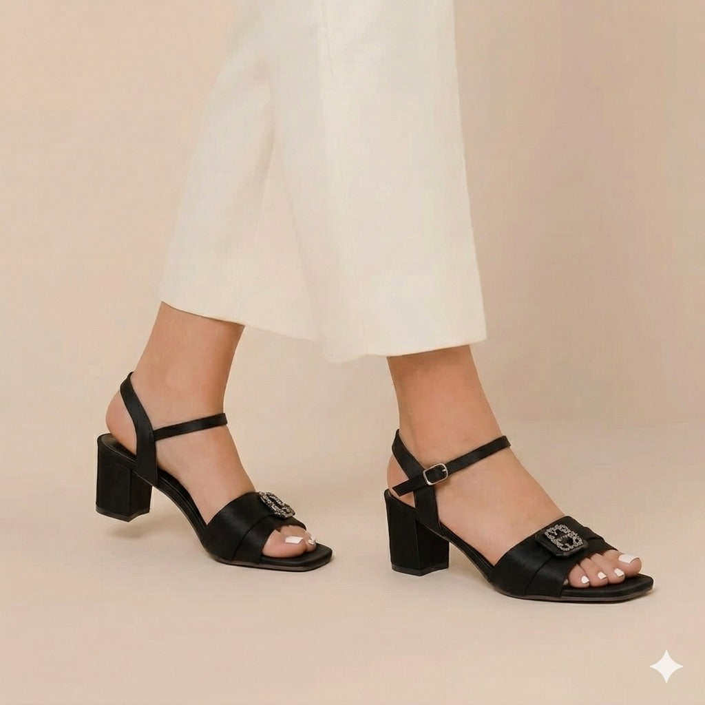 Black block-heel sandals worn with white pants on a beige background