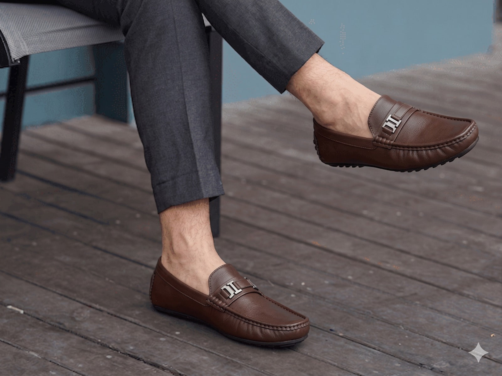 Brown loafers worn with gray pants on a wooden floor.