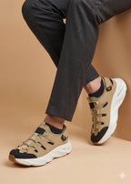 Beige sneakers with black accents worn with dark pants on a beige background