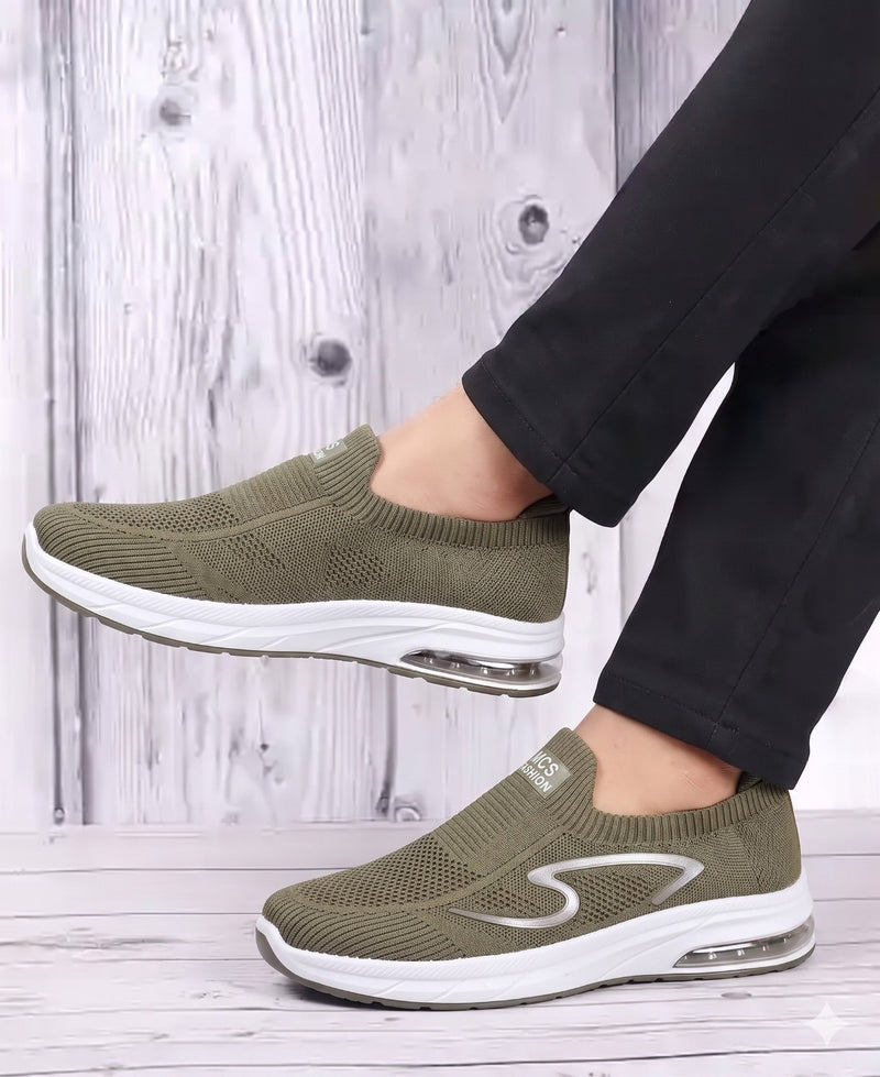 Green slip-on sneakers with white soles worn by a person on a wooden floor.
