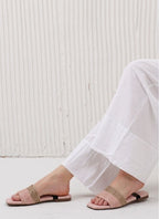 Person wearing pink sandals with gold straps on a light wooden floor.