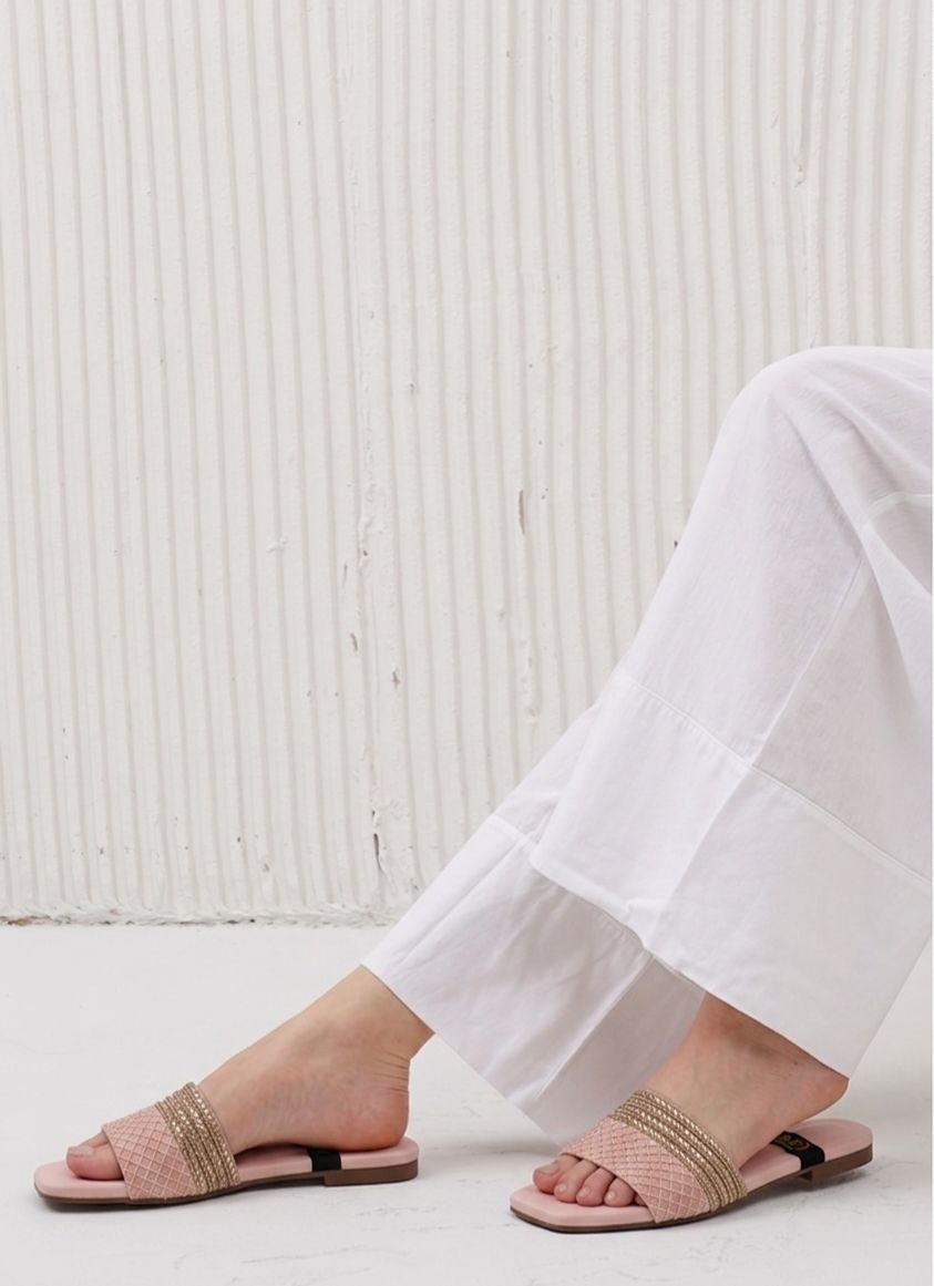 Person wearing pink sandals with gold straps on a light wooden floor.