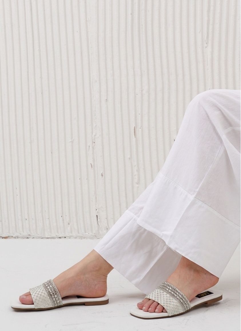 Person wearing white sandals with decorative straps on a light wooden floor.