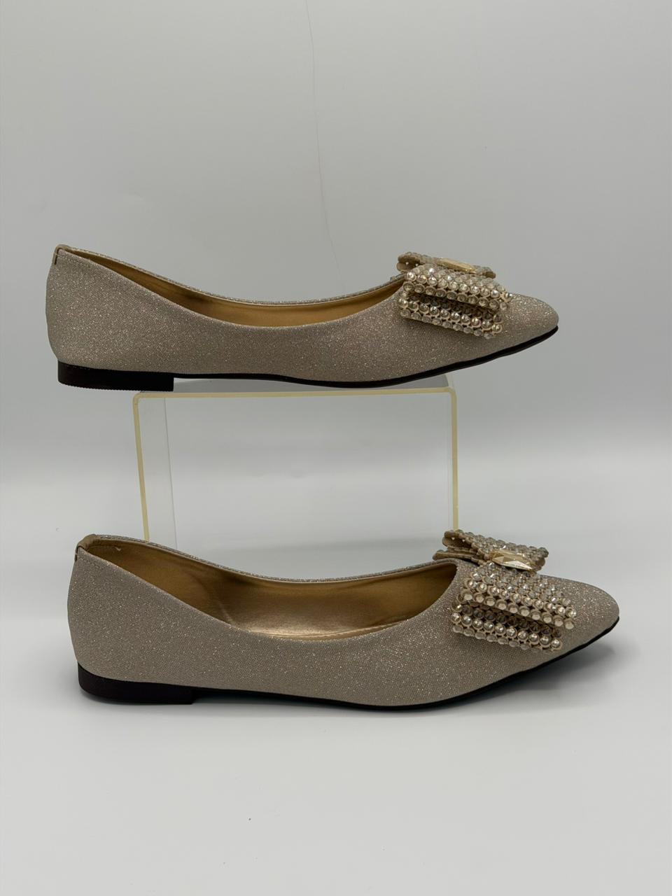 Pair of glittery flats with decorative bow on a white background