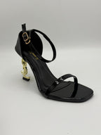 Black high-heeled sandal with gold accents on a gray background