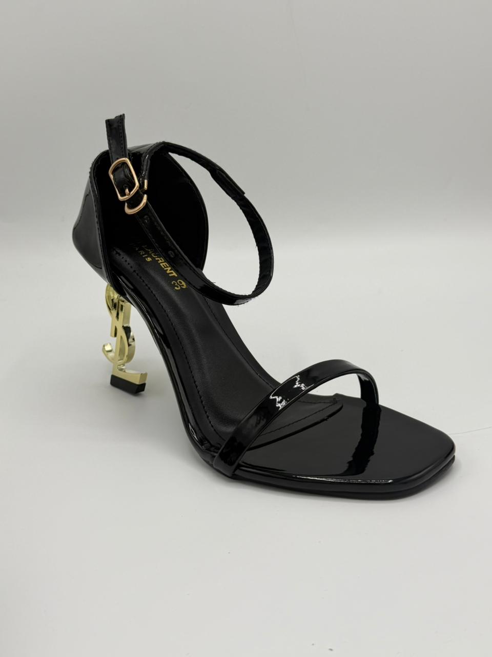 Black high-heeled sandal with gold accents on a gray background