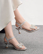 Silver high-heeled sandals with decorative straps on a neutral background