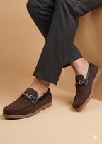 Brown loafers worn with dark pants on a beige background