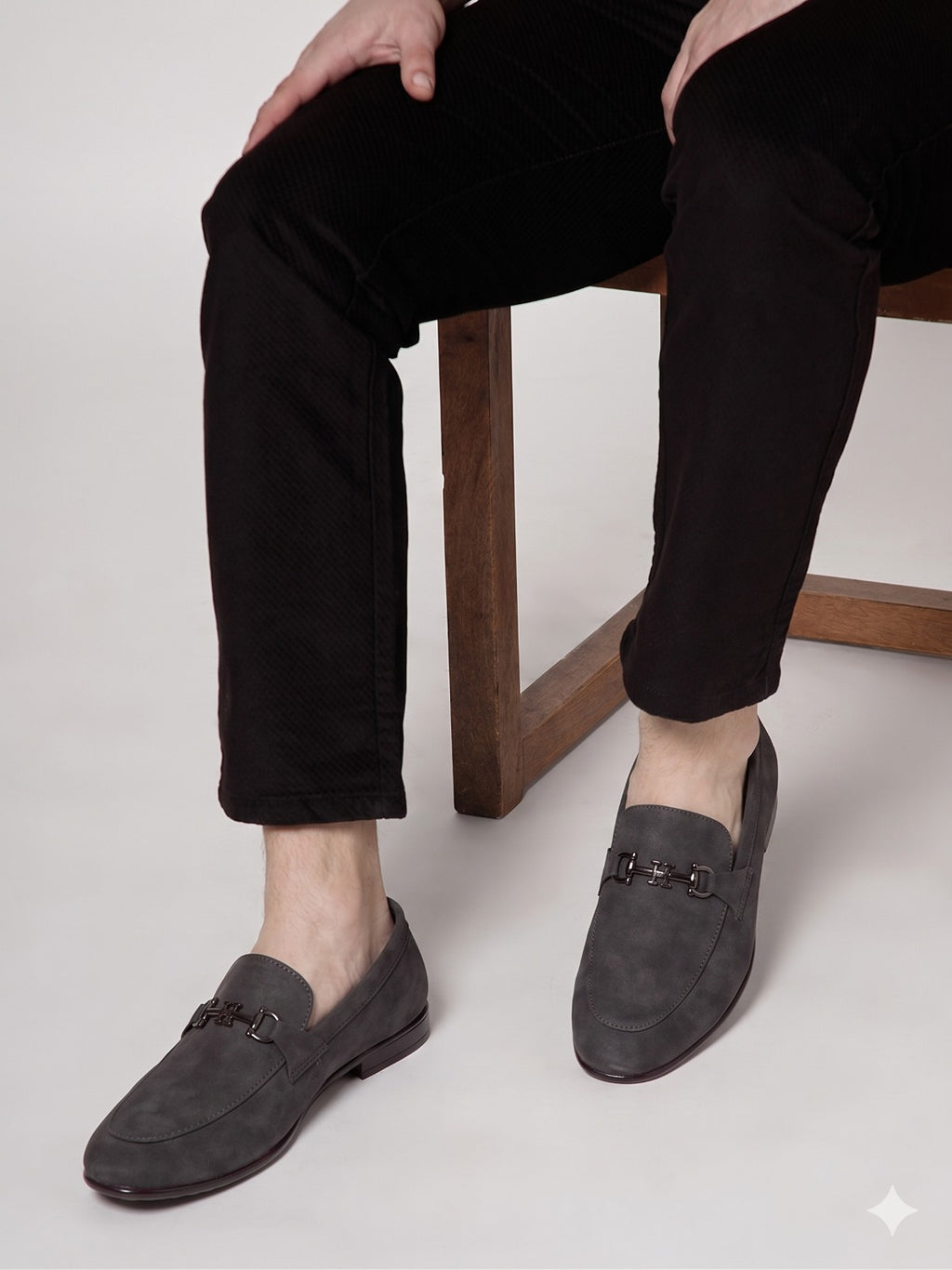Person wearing dark gray loafers with a wooden chair and light background