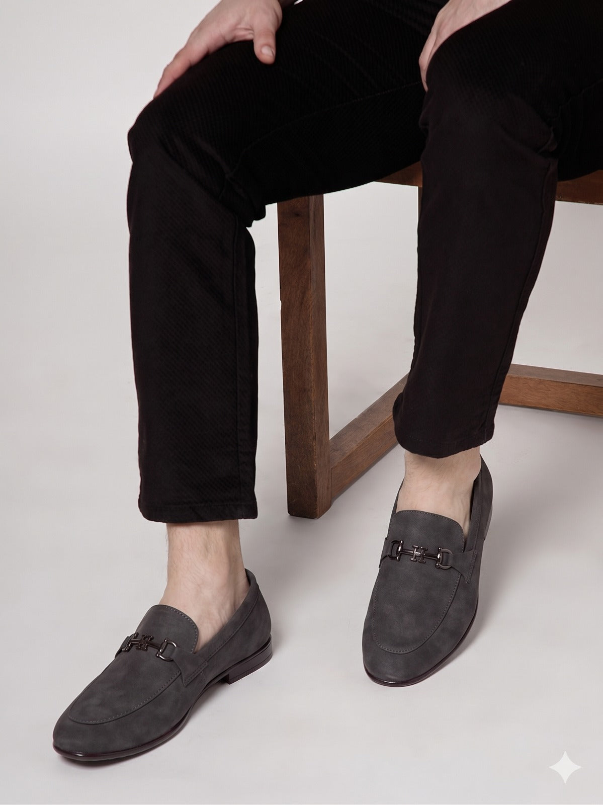 Person wearing dark gray loafers with a wooden chair and light background