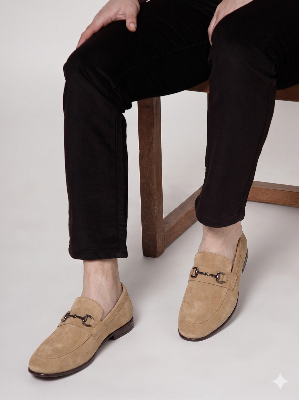 Person wearing beige loafers with a wooden chair and light gray background