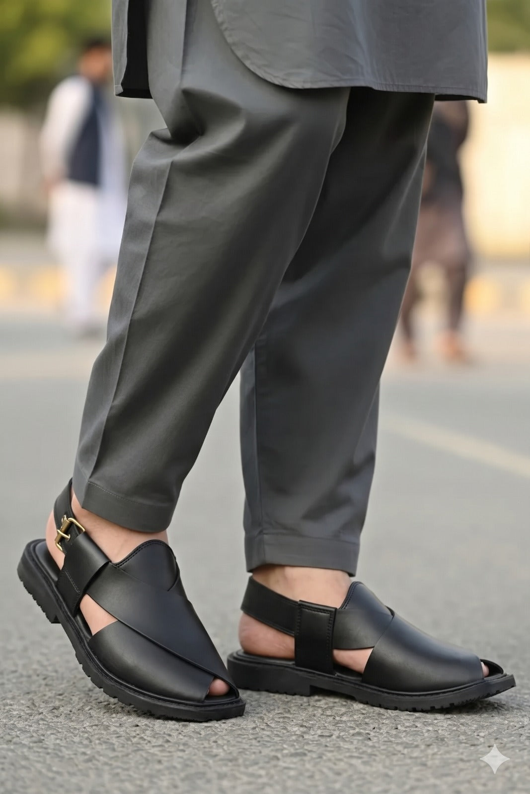 Person wearing black sandals and gray pants on a blurred street background