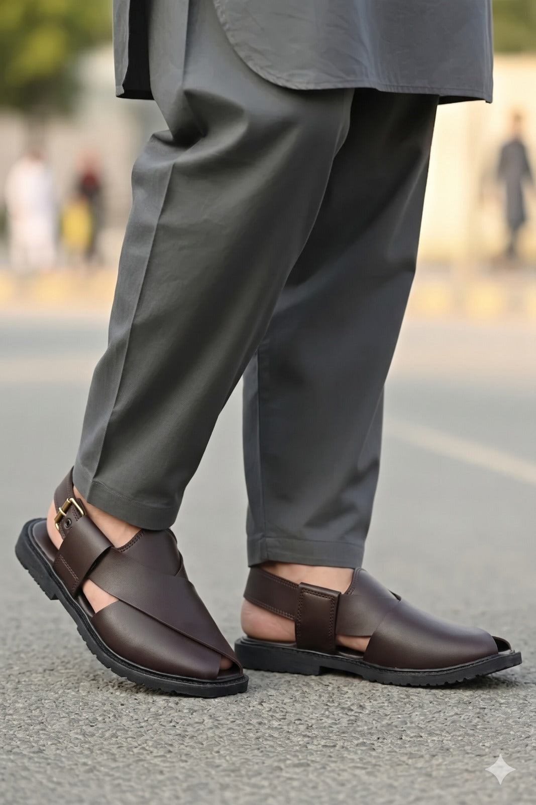 Brown sandals worn with gray pants on a blurred street background