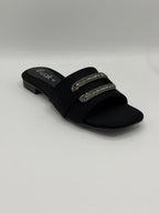 Black slide sandal with embellishments on a light gray background