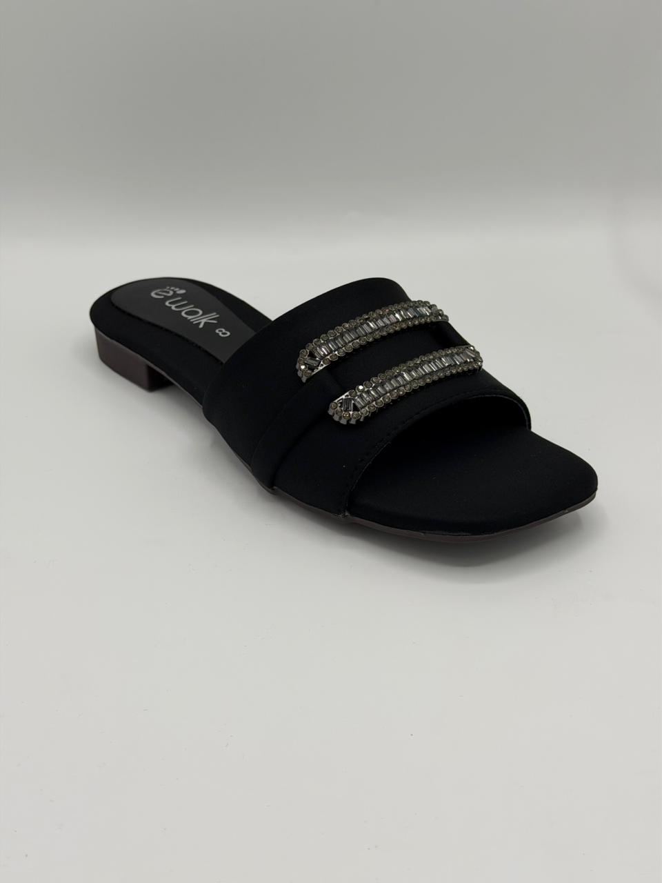 Black slide sandal with embellishments on a light gray background