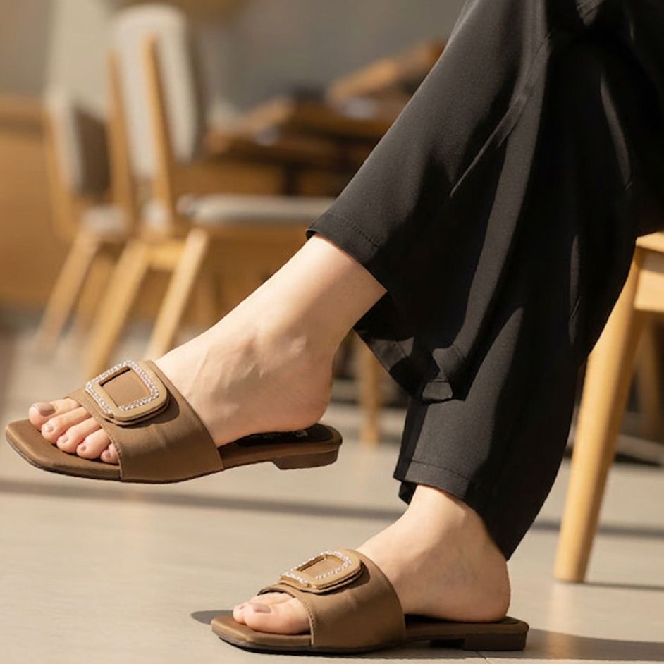 Brown sandals worn with black pants in a blurred indoor setting