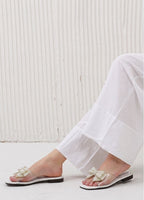 Person wearing white sandals with decorative straps on a light wooden floor.